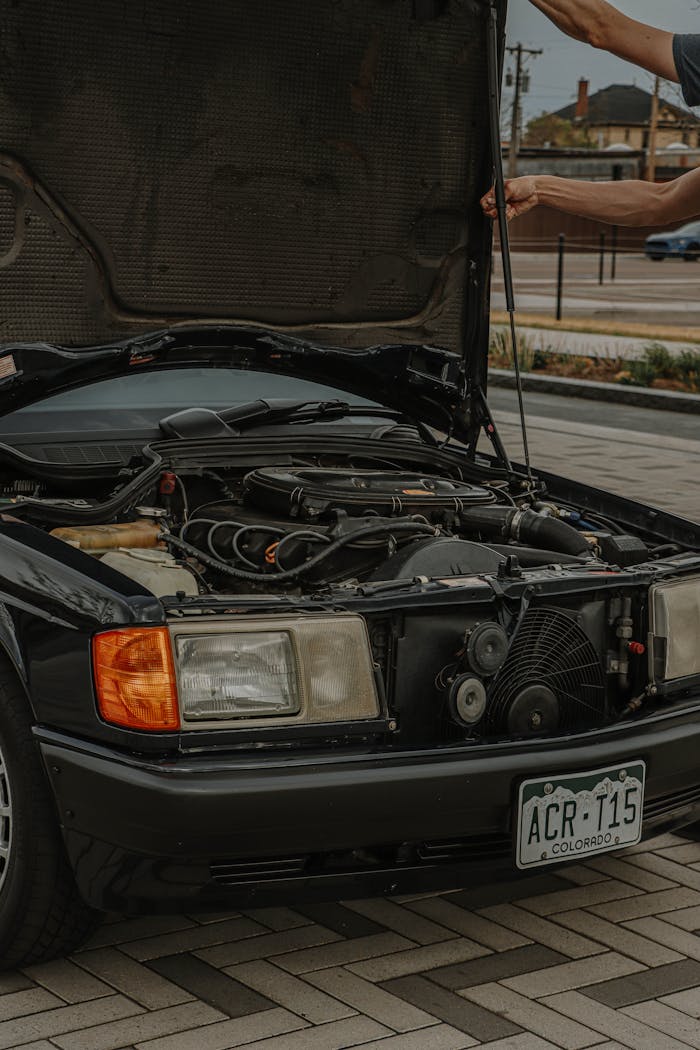 Luxury black car with open hood under inspection, showcasing engine details.